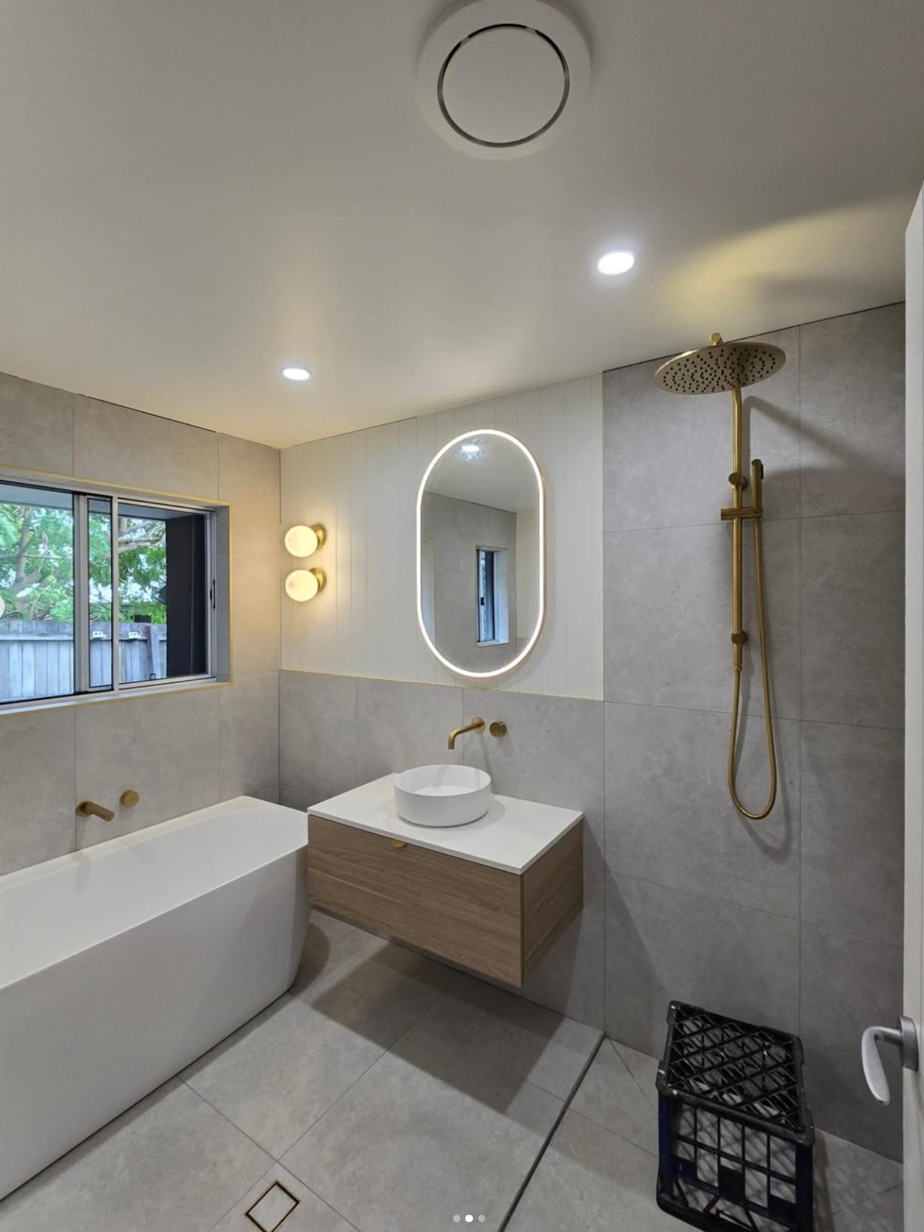 Oval LED mirror, wall sconces, freestanding bath and gold fittings — bathroom renovation Noosa
