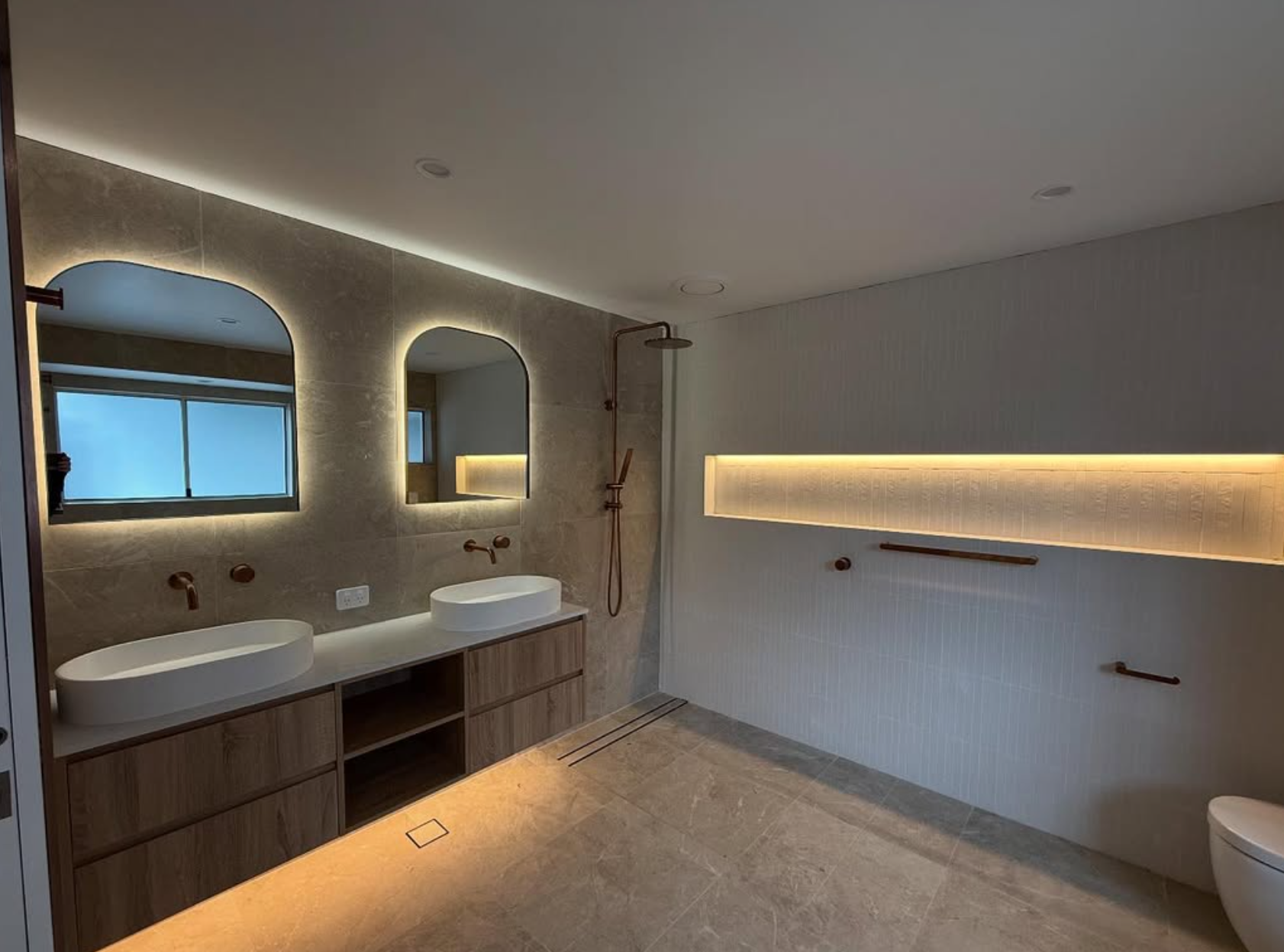 Double arched LED backlit mirrors with rose gold tapware and LED strip shower niche — luxury ensuite