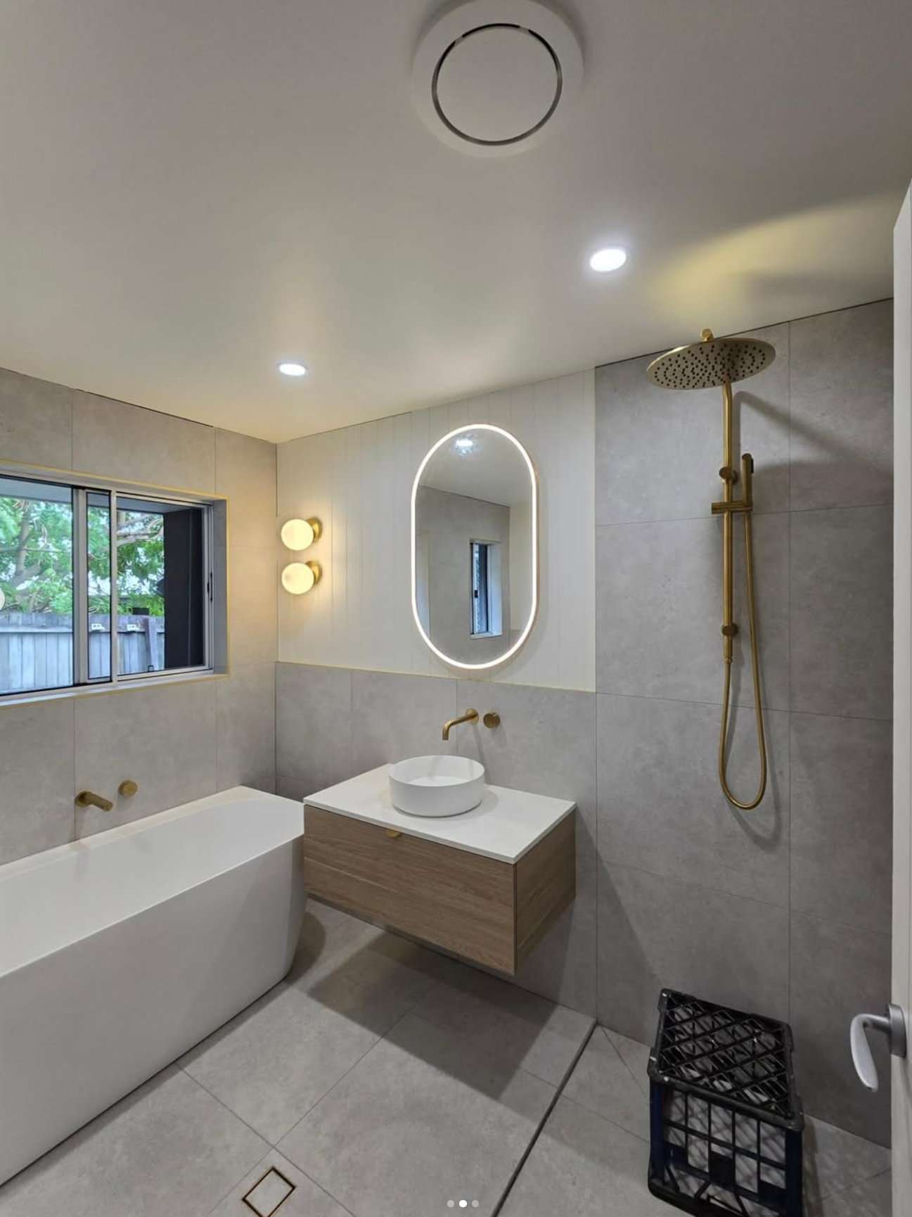 Oval LED mirror, wall sconces, freestanding bath and gold fittings — bathroom renovation Noosa