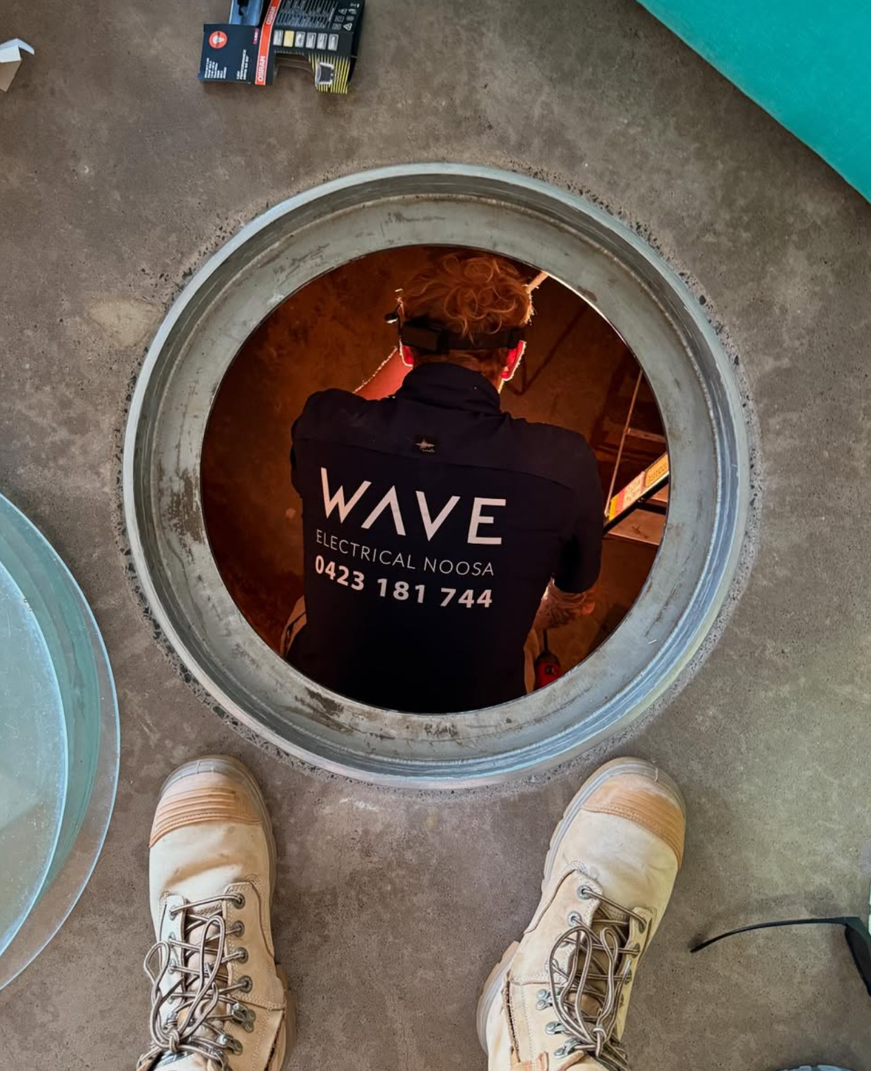 Wave Electrical technician working inside an underground access pit — underground electrical installation